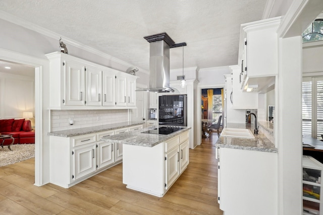 kitchen with light wood finished floors, black electric stovetop, island range hood, white cabinetry, and a sink