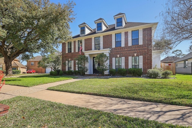 colonial inspired home with a front lawn, fence, and brick siding