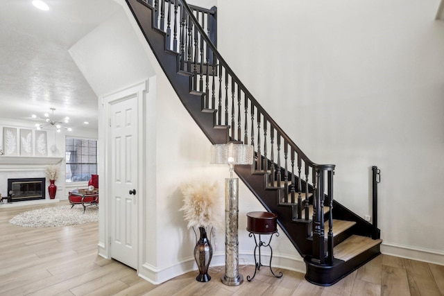 staircase with a glass covered fireplace, wood finished floors, and baseboards