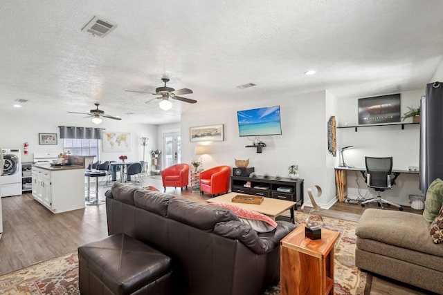 living room with visible vents, washer / clothes dryer, a textured ceiling, baseboards, and dark wood-style flooring