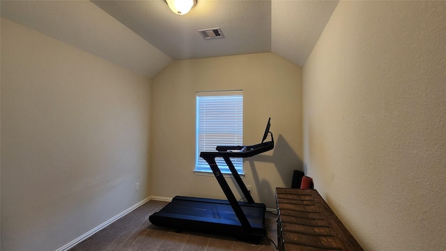 exercise area featuring visible vents, carpet floors, baseboards, vaulted ceiling, and a textured wall