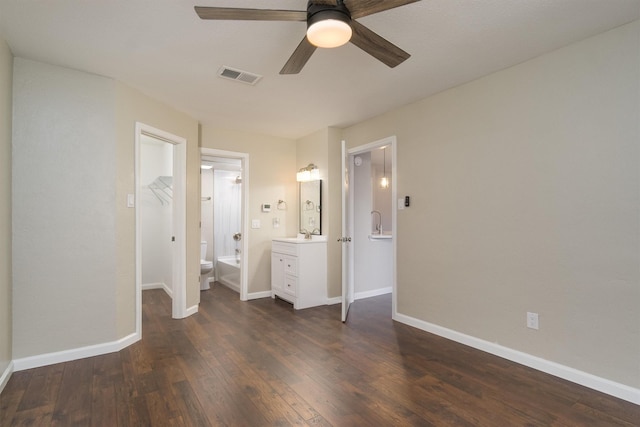 unfurnished bedroom featuring dark wood-style floors, visible vents, ensuite bath, and baseboards