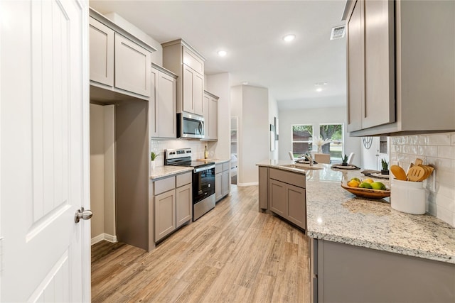 kitchen with light wood-type flooring, decorative backsplash, appliances with stainless steel finishes, and gray cabinetry