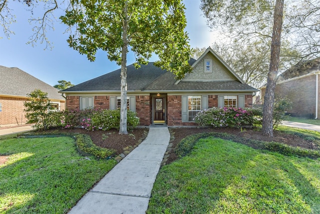 view of front facade with brick siding, a shingled roof, and a front lawn