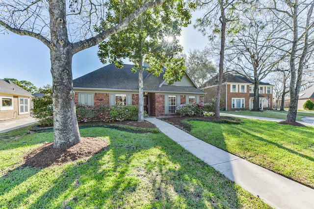 view of front of home with brick siding, roof with shingles, and a front yard