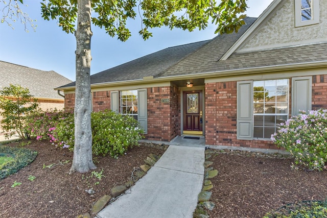 doorway to property with brick siding and roof with shingles