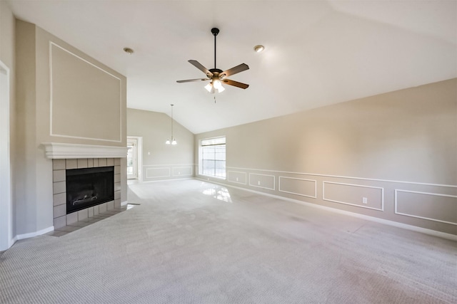 unfurnished living room featuring a ceiling fan, carpet floors, lofted ceiling, a tile fireplace, and a decorative wall