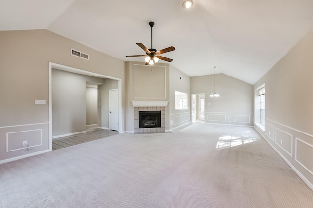 unfurnished living room featuring visible vents, light carpet, a tiled fireplace, a decorative wall, and vaulted ceiling