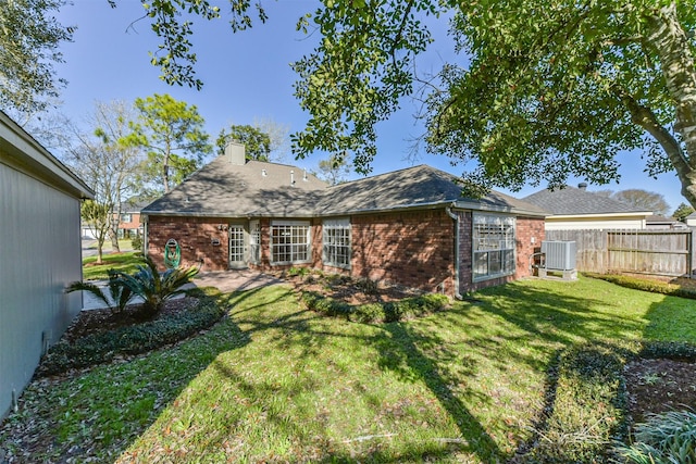 back of house with central AC, fence, a yard, brick siding, and a chimney