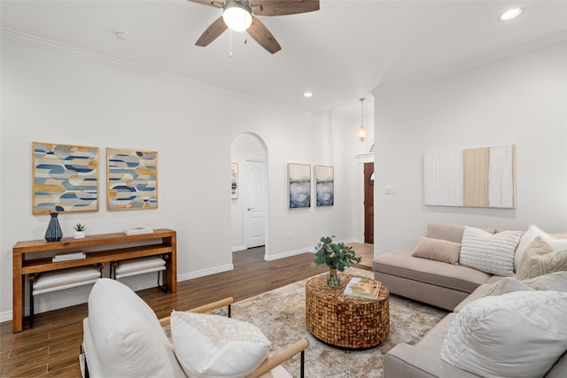 living room featuring crown molding, baseboards, wood finished floors, arched walkways, and a ceiling fan