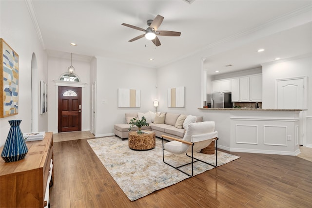 living area featuring arched walkways, crown molding, ceiling fan, and wood finished floors