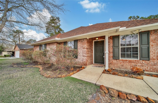 view of exterior entry with a yard, brick siding, and roof with shingles