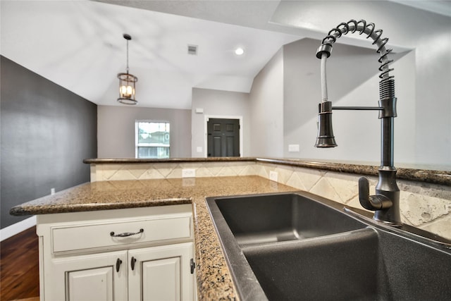 kitchen featuring dark stone counters, dark wood-style flooring, a sink, vaulted ceiling, and decorative light fixtures