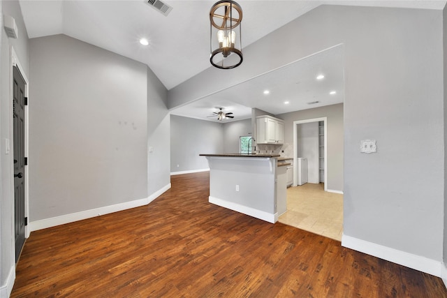 kitchen with dark countertops, visible vents, lofted ceiling, wood finished floors, and white cabinetry