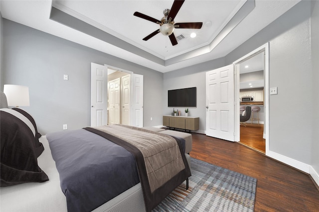 bedroom featuring visible vents, baseboards, a tray ceiling, wood finished floors, and a ceiling fan