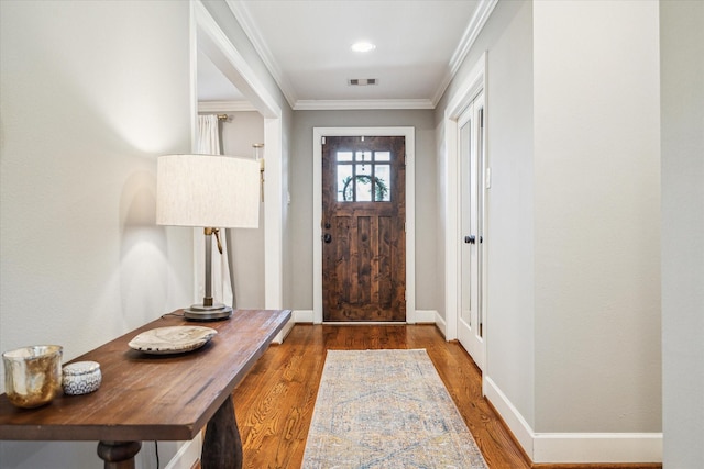 entryway with crown molding, wood finished floors, visible vents, and baseboards