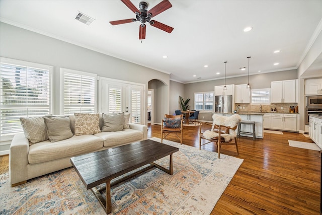 living area featuring wood finished floors, visible vents, arched walkways, and ornamental molding