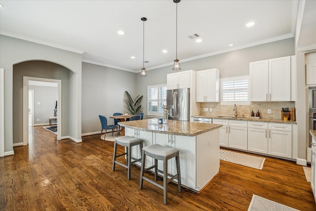 kitchen featuring visible vents, arched walkways, dark wood-type flooring, appliances with stainless steel finishes, and a center island