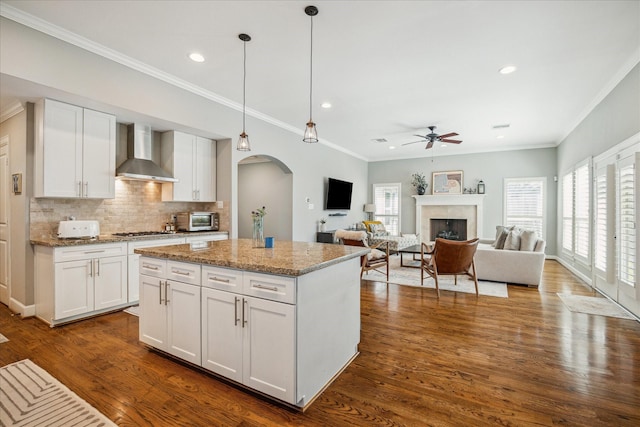 kitchen featuring dark wood-type flooring, wall chimney range hood, stainless steel gas cooktop, a fireplace, and arched walkways