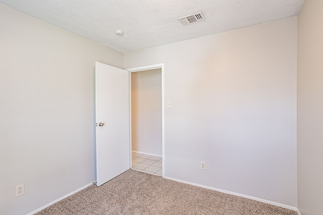 spare room with visible vents, baseboards, light colored carpet, and a textured ceiling