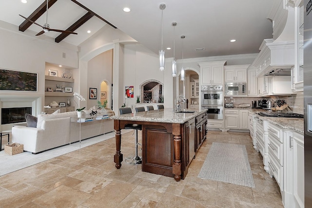 kitchen with premium range hood, a sink, a glass covered fireplace, stainless steel appliances, and arched walkways