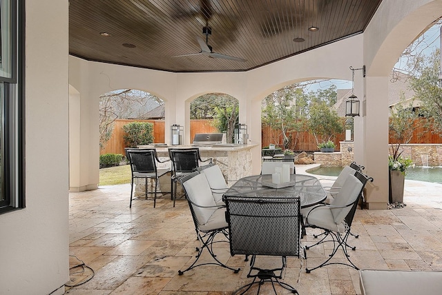 view of patio featuring outdoor wet bar, outdoor dining area, a fenced backyard, an outdoor kitchen, and a ceiling fan