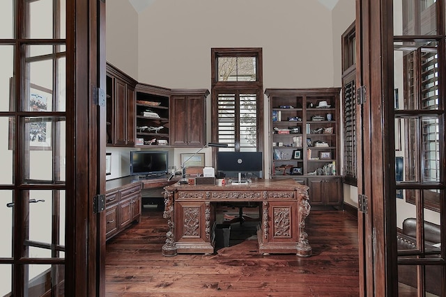 office space featuring dark wood finished floors, built in desk, and a towering ceiling