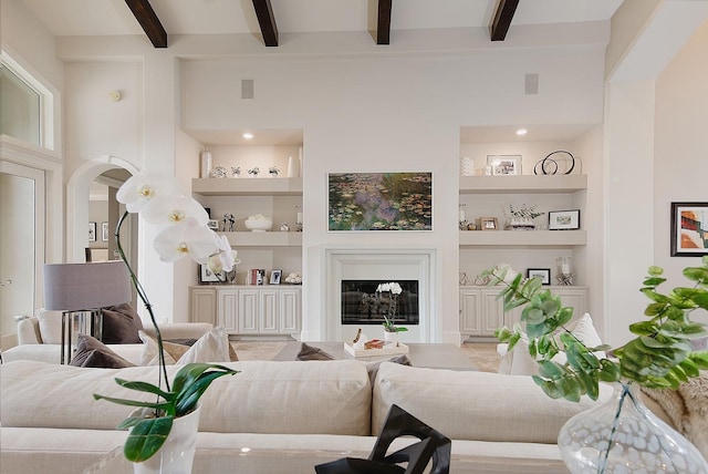 living room with a glass covered fireplace, beamed ceiling, built in features, and visible vents