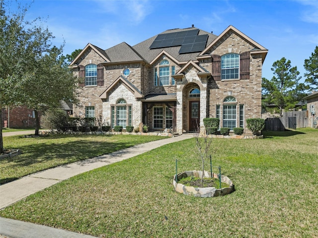 view of front facade featuring brick siding, solar panels, a front yard, and fence