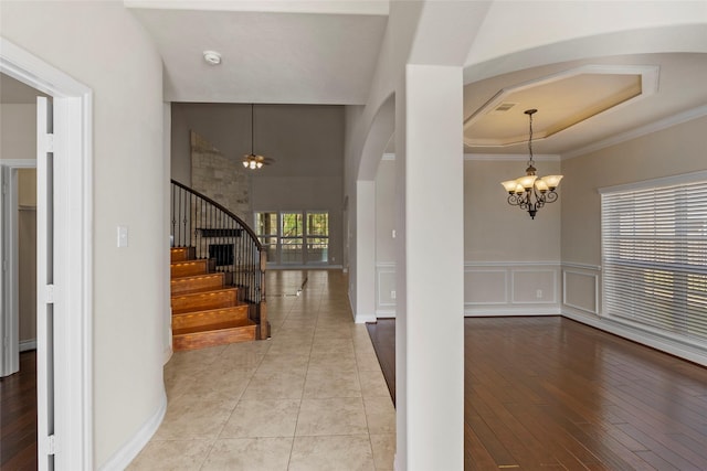 entrance foyer with stairway, a tray ceiling, wood finished floors, arched walkways, and a notable chandelier