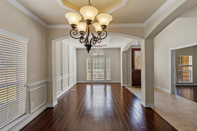 unfurnished dining area with baseboards, a chandelier, wood finished floors, arched walkways, and a raised ceiling