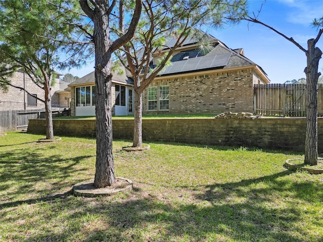 rear view of house featuring solar panels, fence, a lawn, and brick siding