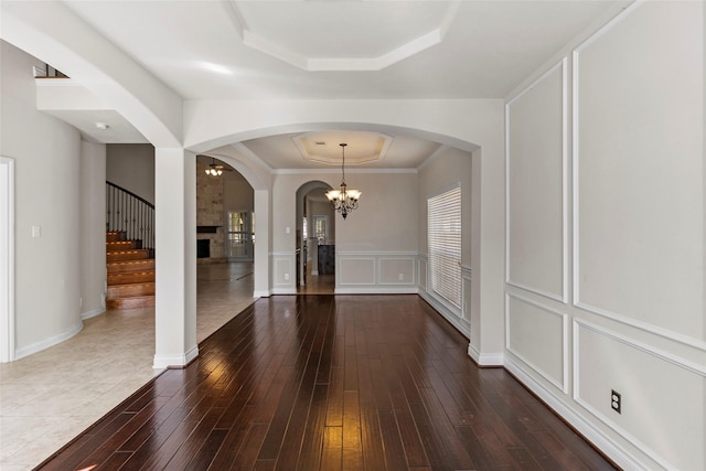 interior space with a tray ceiling, arched walkways, dark wood-type flooring, and a decorative wall