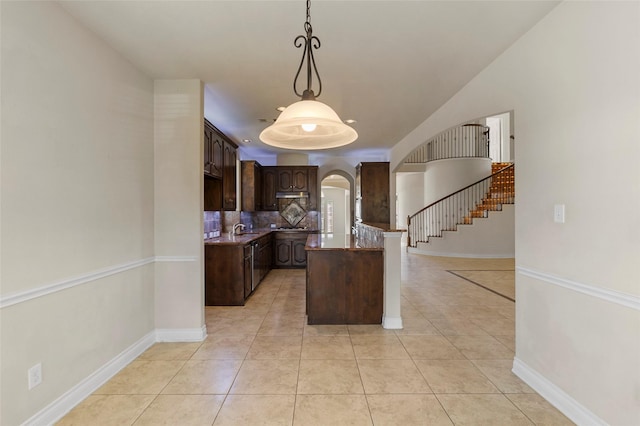 kitchen featuring a peninsula, light tile patterned flooring, arched walkways, dark brown cabinetry, and backsplash