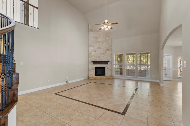 unfurnished living room with high vaulted ceiling, a ceiling fan, arched walkways, a stone fireplace, and baseboards