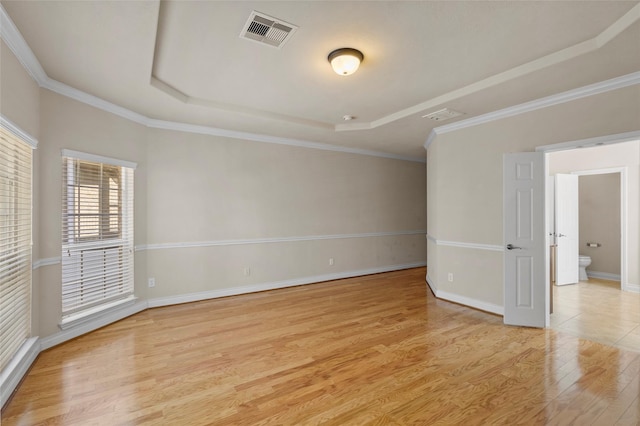 empty room with baseboards, visible vents, light wood finished floors, ornamental molding, and a raised ceiling