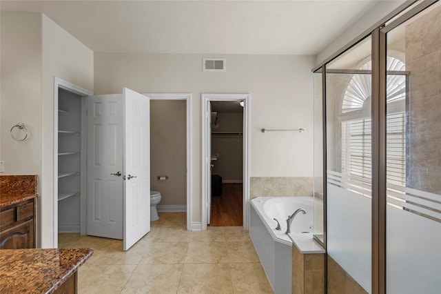 bathroom featuring visible vents, a walk in closet, a garden tub, toilet, and tile patterned floors