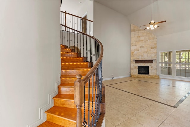 staircase with high vaulted ceiling, a fireplace, tile patterned flooring, baseboards, and ceiling fan