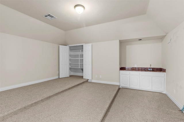 spare room featuring baseboards, visible vents, indoor wet bar, vaulted ceiling, and light carpet