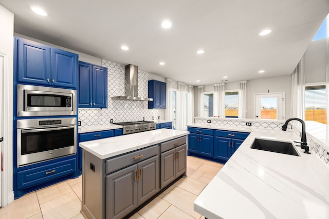 kitchen with a center island, wall chimney range hood, decorative backsplash, appliances with stainless steel finishes, and a sink