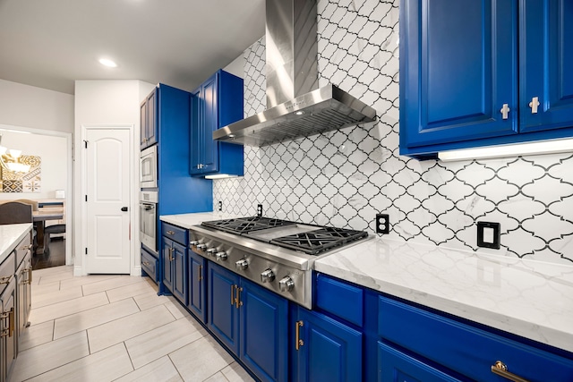 kitchen with blue cabinets, light stone counters, stainless steel appliances, wall chimney exhaust hood, and decorative backsplash