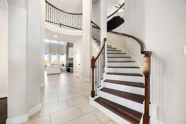 staircase featuring baseboards, a high ceiling, a lit fireplace, and tile patterned flooring