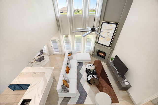 living room featuring tile patterned flooring, a warm lit fireplace, baseboards, and a ceiling fan