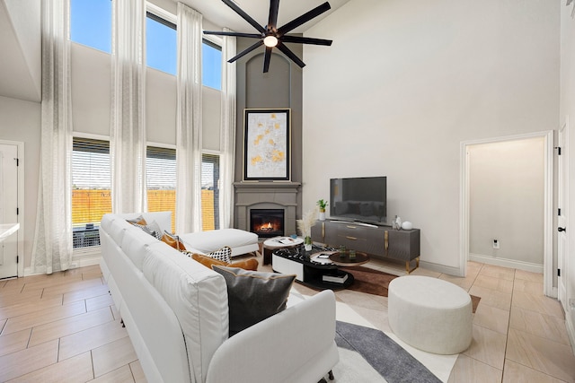 living area featuring ceiling fan, baseboards, a high ceiling, and a glass covered fireplace