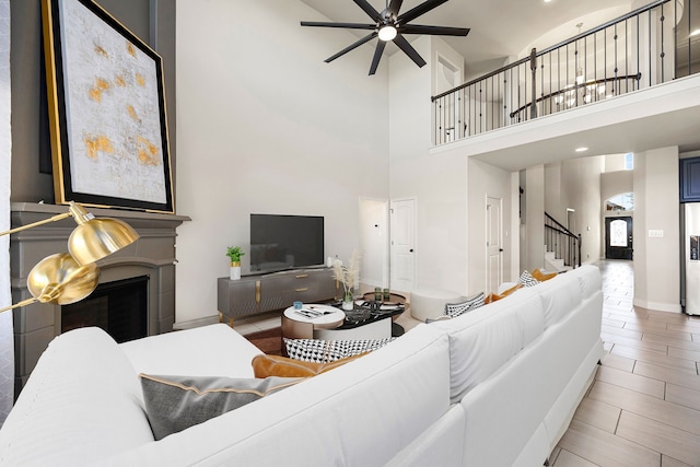 living room with baseboards, a fireplace, ceiling fan, stairs, and a towering ceiling