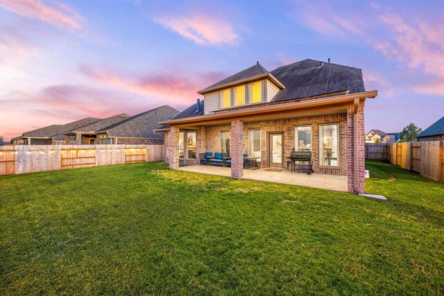 back of property at dusk with a patio, a fenced backyard, brick siding, and a lawn