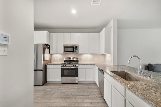 kitchen featuring light stone countertops, visible vents, a sink, appliances with stainless steel finishes, and backsplash