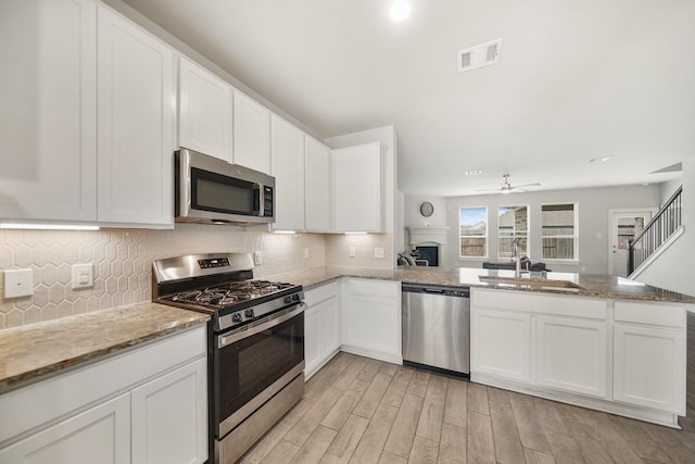 kitchen with visible vents, a peninsula, a sink, white cabinets, and appliances with stainless steel finishes