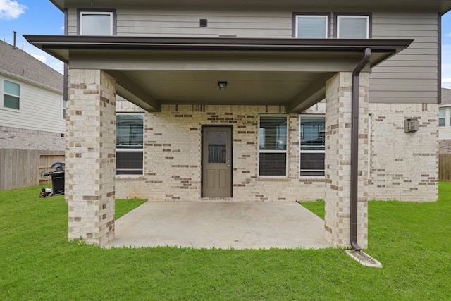 view of exterior entry featuring brick siding, a patio, a yard, and fence