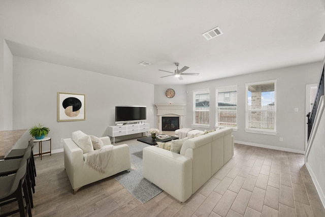 living area featuring light wood finished floors, visible vents, baseboards, ceiling fan, and a glass covered fireplace